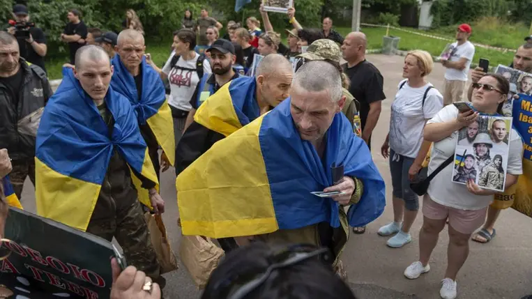 Hazatérő ukrán katonák a nemzeti zászlóval a vállukon, családtagjaik a fogságban tartottak portréival várják őket a csernyihivi régióban, 2025. július 4-én. Forrás: AFP