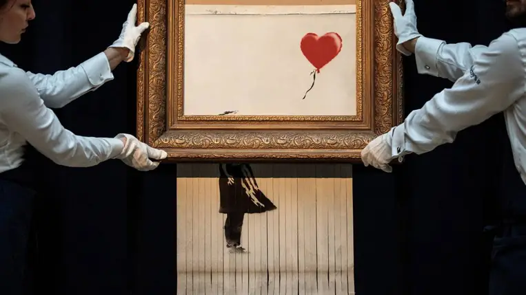 A Sotheby's alkalmazottai a brit művész, Banksy „Love is in the Bin” című műve mellett a Sotheby's aukciós házban 2018. október 12-én, Londonban. Fotó: Jack Taylor / Getty Images